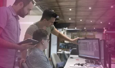 Three people collaborating at a computer in a modern office.