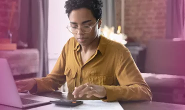 Person using a laptop and calculator at a desk with a focused expression.