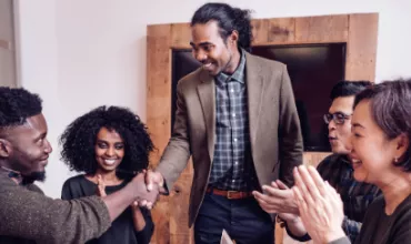 Smiling colleagues clapping as two people shake hands in an office.