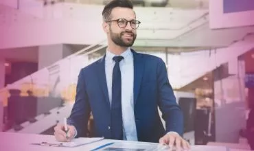 Person in business attire smiling while working at a desk.